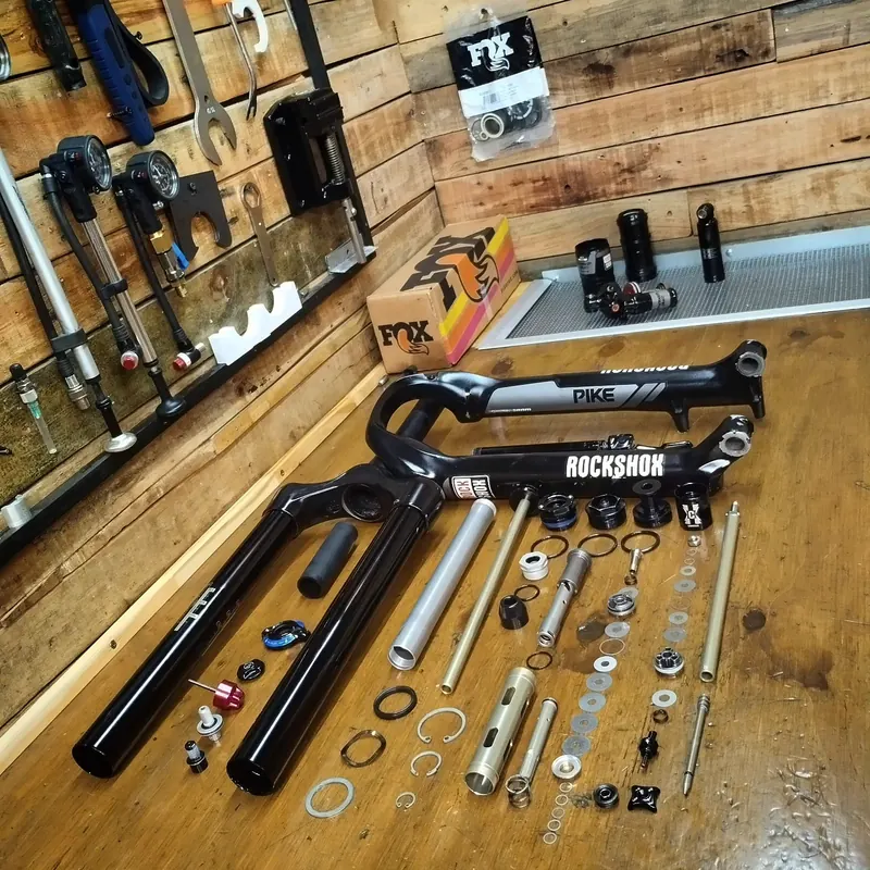 Horquilla RockShox Pike completamente desarmada, con sus piezas ordenadas sobre el banco de madera.
